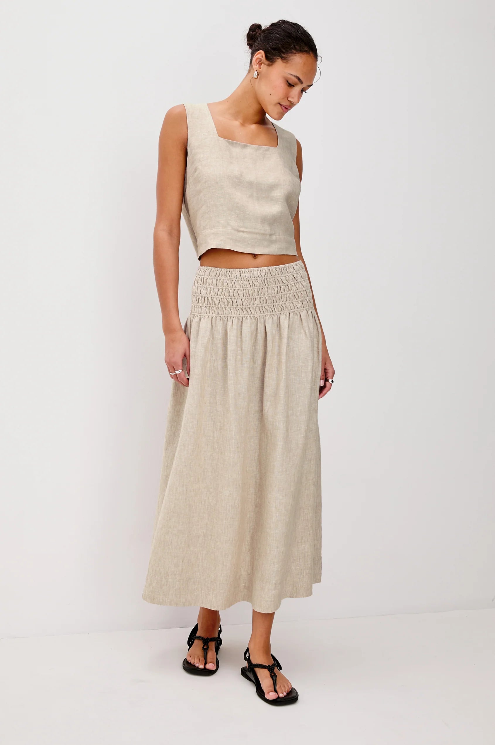 Woman wearing a beige sleeveless top and long skirt on a white background
