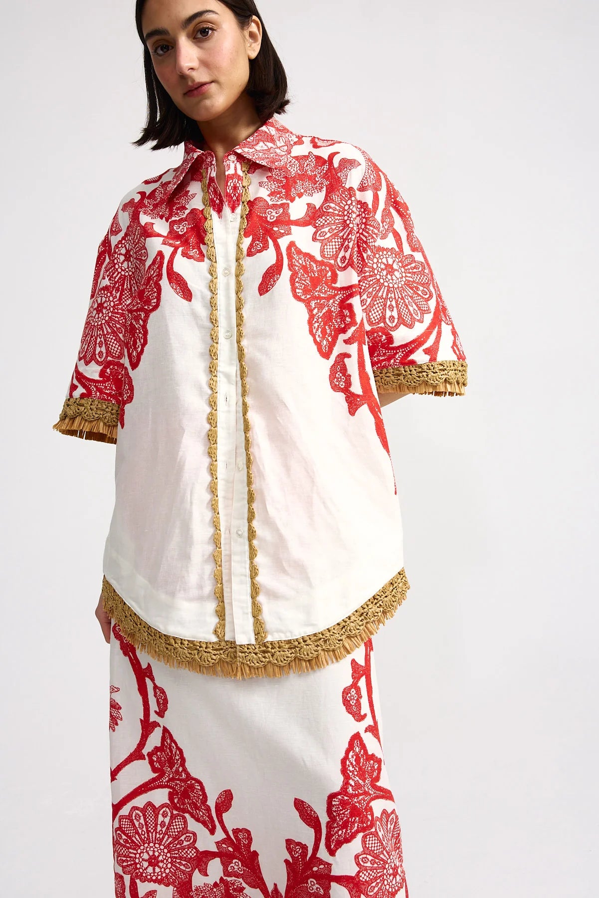 Woman wearing a white and red patterned outfit with gold accents on a white background