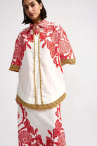 Woman wearing a white and red patterned outfit with gold accents on a white background