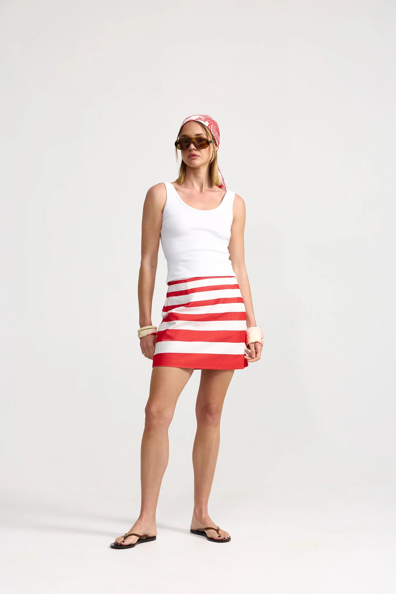 Woman wearing a white tank top and red and white striped skirt on a white background