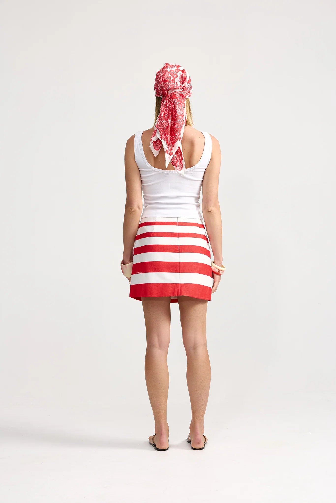 Person wearing a white tank top and red and white striped skirt with a headscarf on a white background