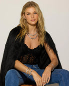 Woman wearing a black top and blue jeans with jewelry against a plain background