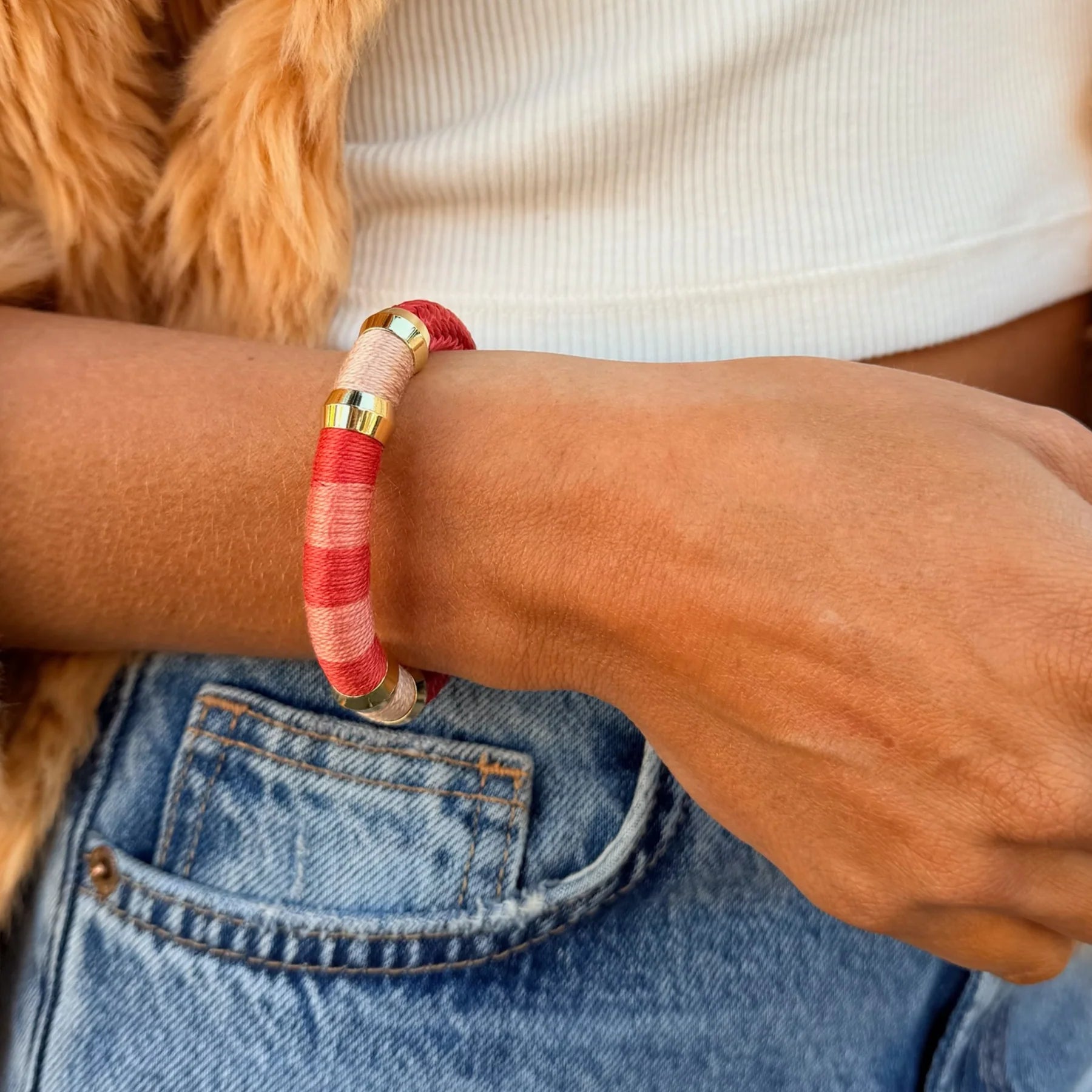 Person wearing a red and gold bracelet on a casual outfit with a dog in the background