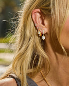 Close-up of a person's ear with multiple earrings and a blurred outdoor background