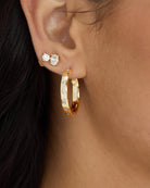 Close-up of an ear wearing gold hoop earrings with small diamonds.