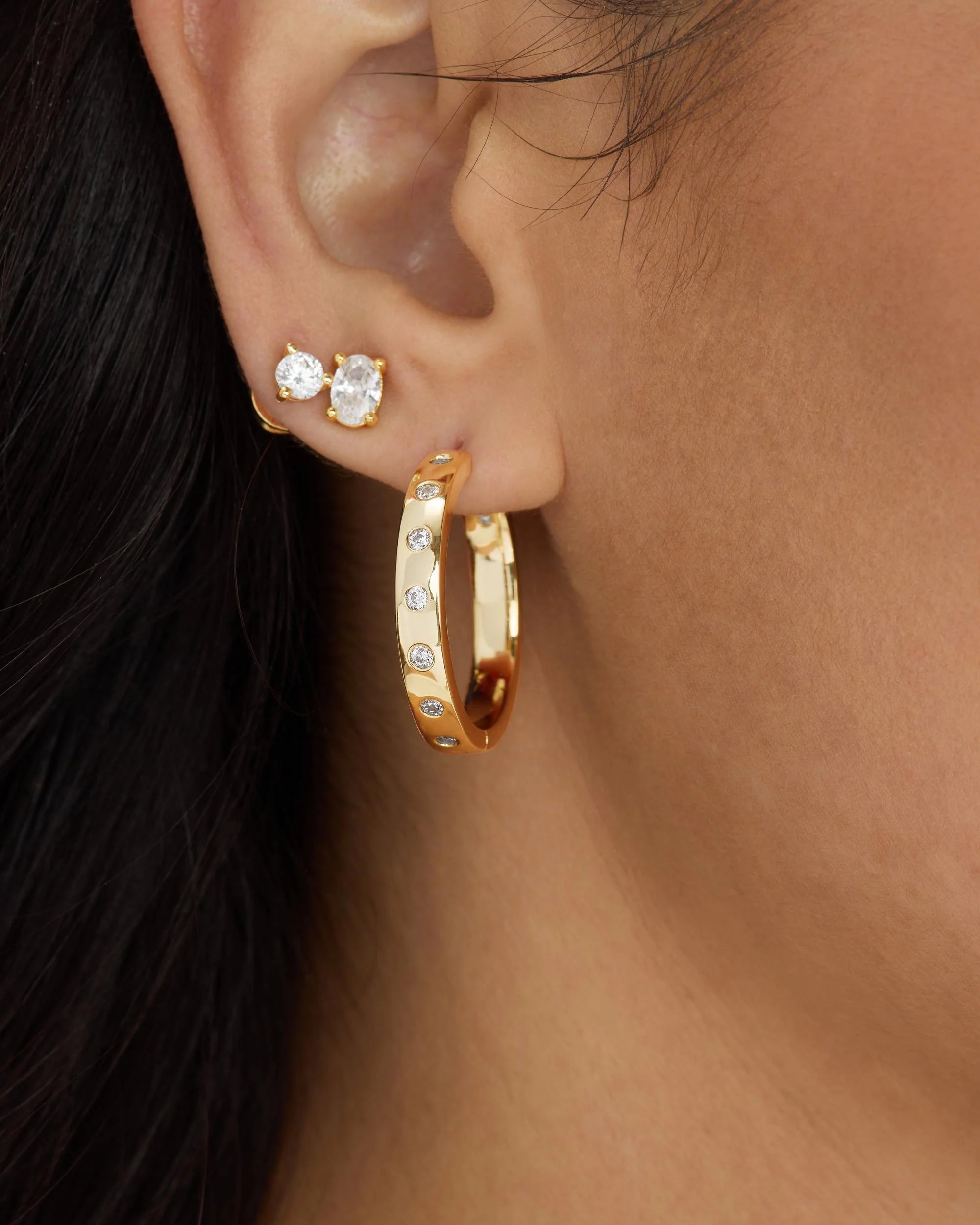 Close-up of an ear wearing gold hoop earrings with small diamonds.