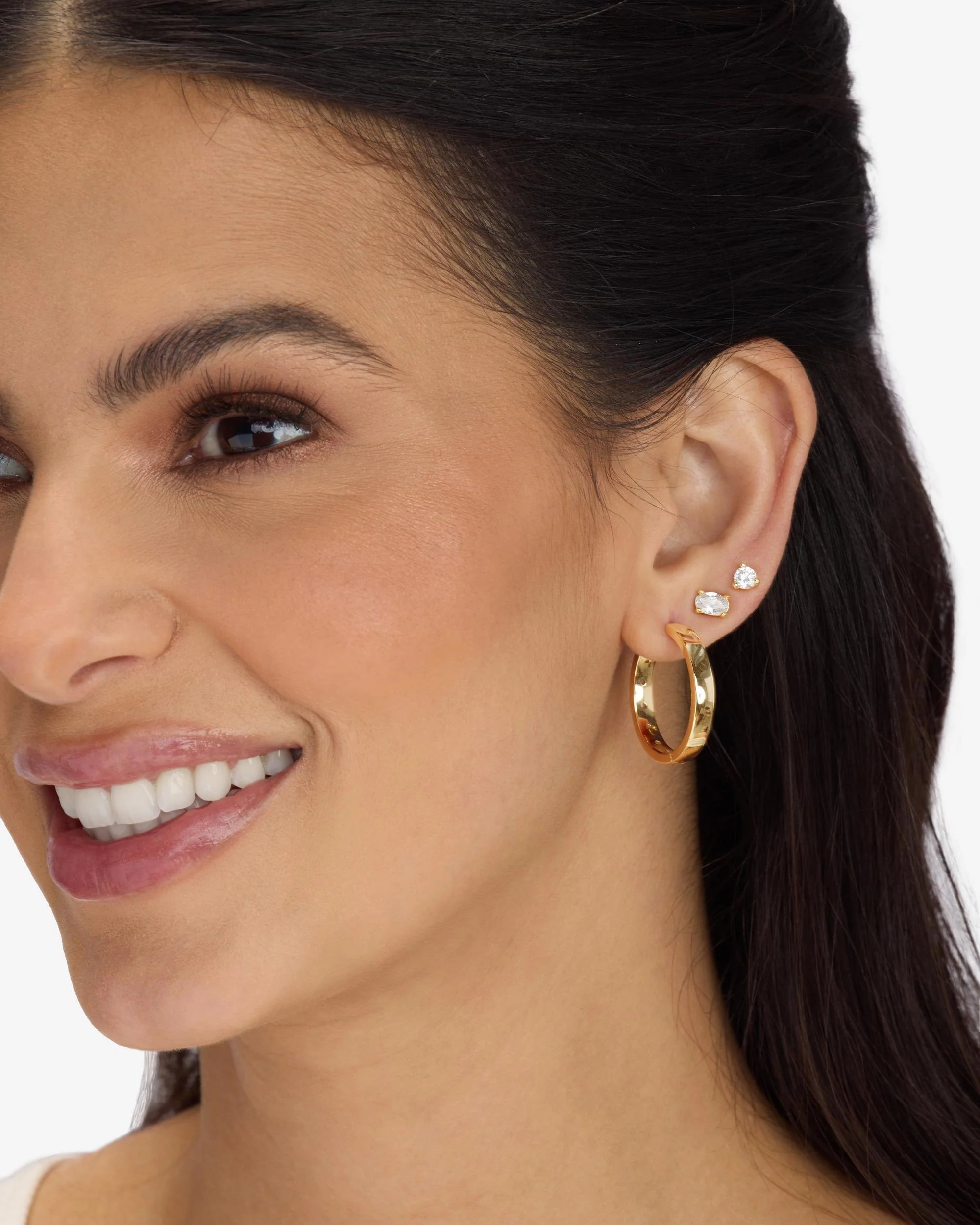 Close-up of a woman wearing gold hoop earrings with small diamond-like stones.