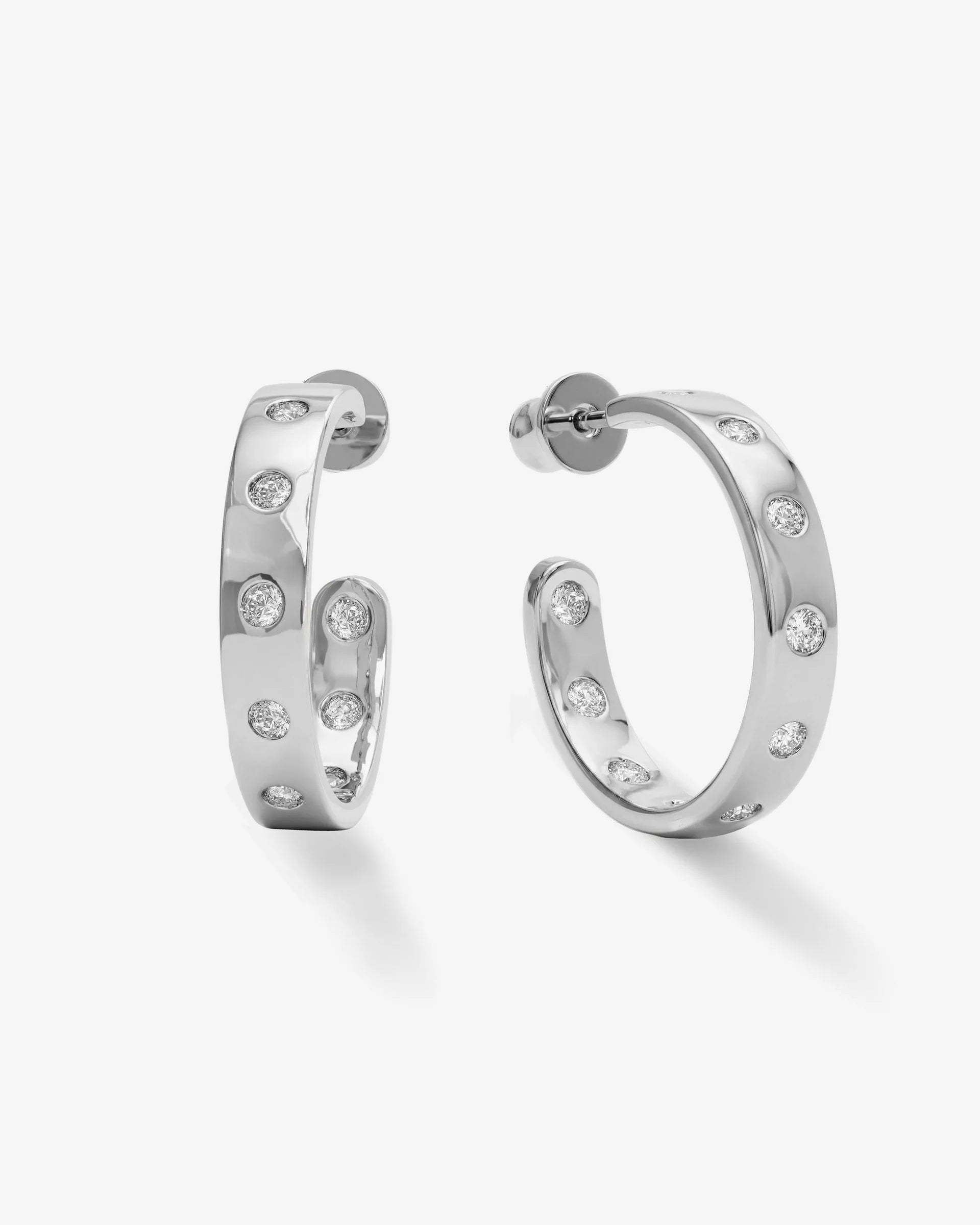 A pair of silver hoop earrings with small clear round-cut stones set along the front, shown on a clean light gray background.