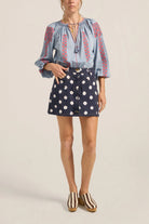 Woman wearing a blue embroidered blouse and navy shorts with white polka dots on a beige background