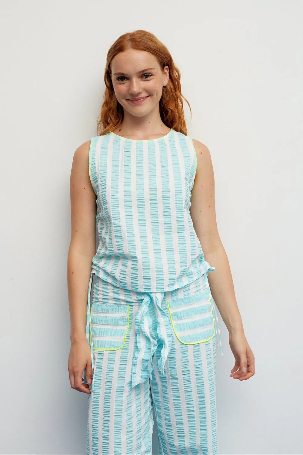 Woman wearing a light blue and white striped sleeveless top and pants set against a plain background.