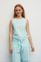 Woman wearing a light blue and white striped sleeveless top and pants set against a plain background.