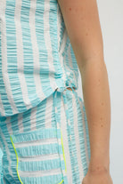 Close-up of a person wearing a light blue and white striped dress with ruffled details on a plain background.