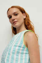 Woman wearing a light blue and white striped sleeveless top against a plain background