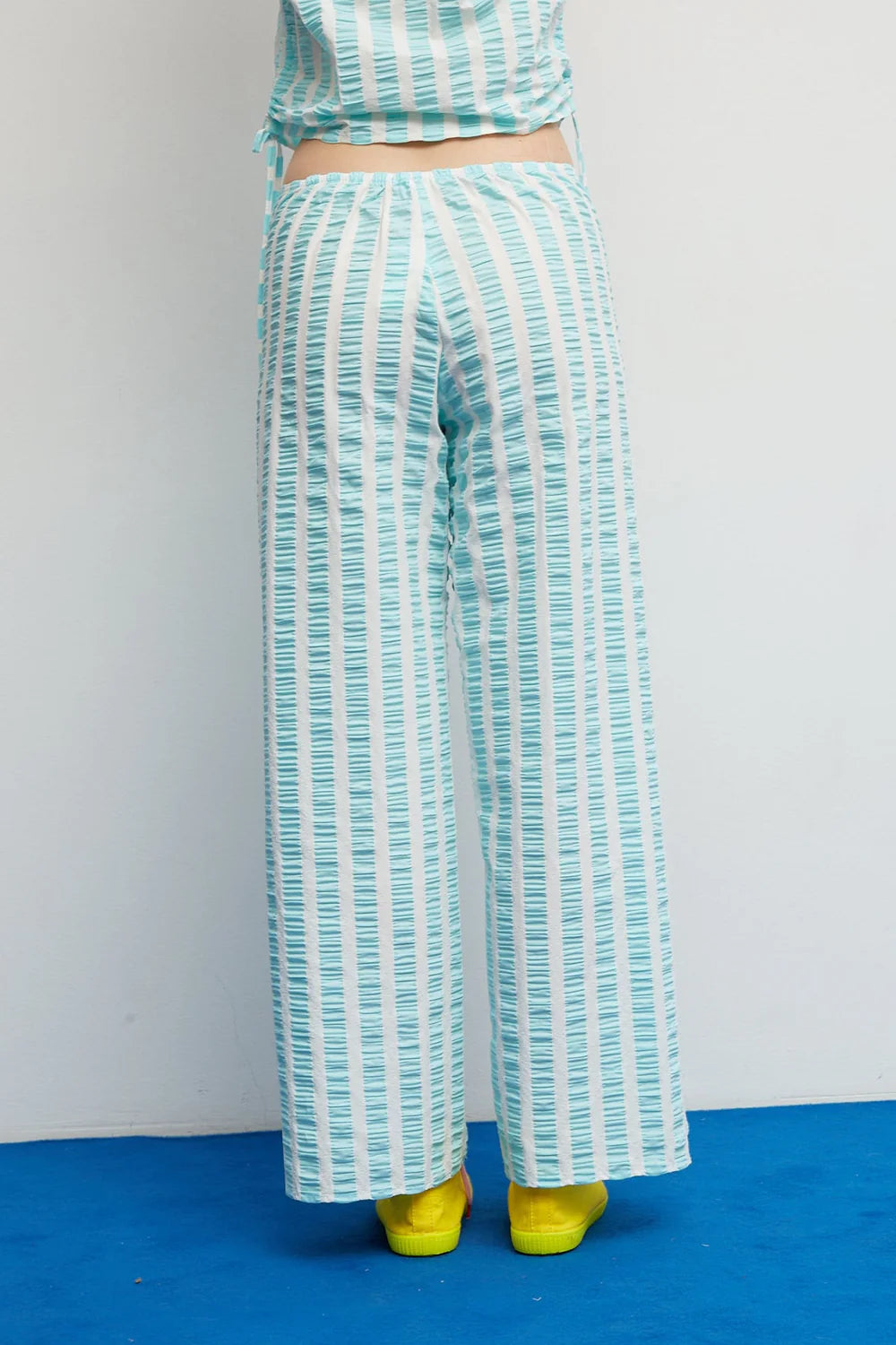 Teal and white striped outfit with yellow shoes on a blue floor against a white wall