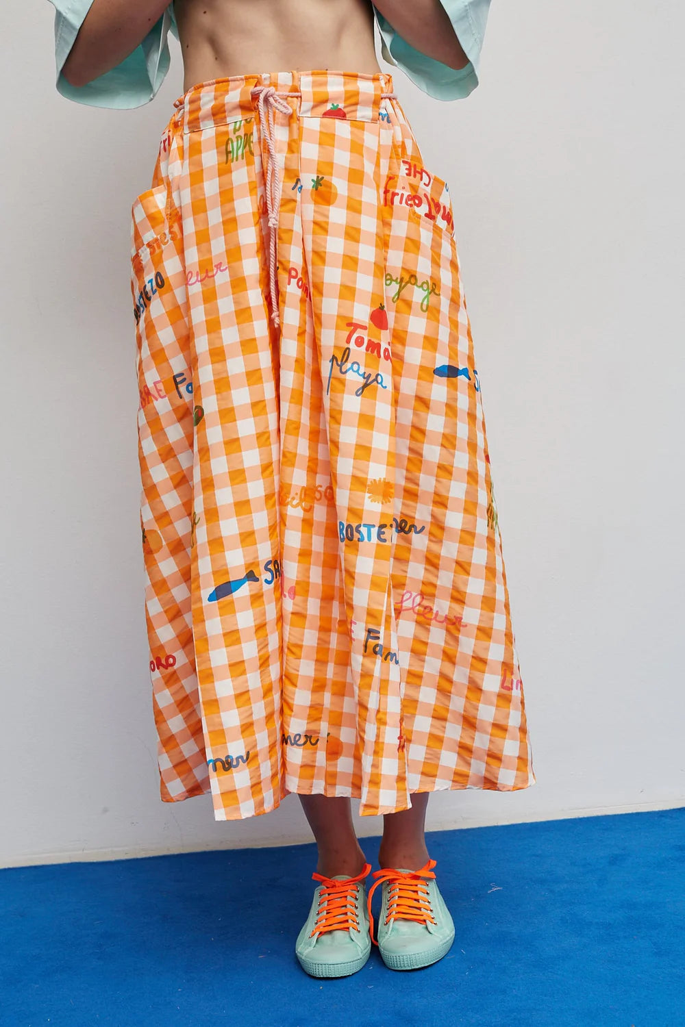 Person wearing an orange checkered skirt with text and a blue shirt on a white background