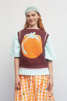 Child wearing a sweater vest with a pumpkin design on a plain background