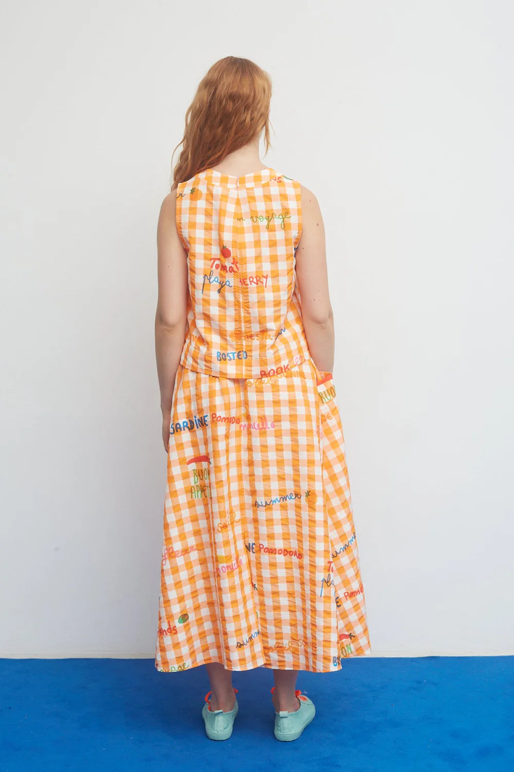 Woman wearing a long orange checkered dress with colorful text patterns on a white background