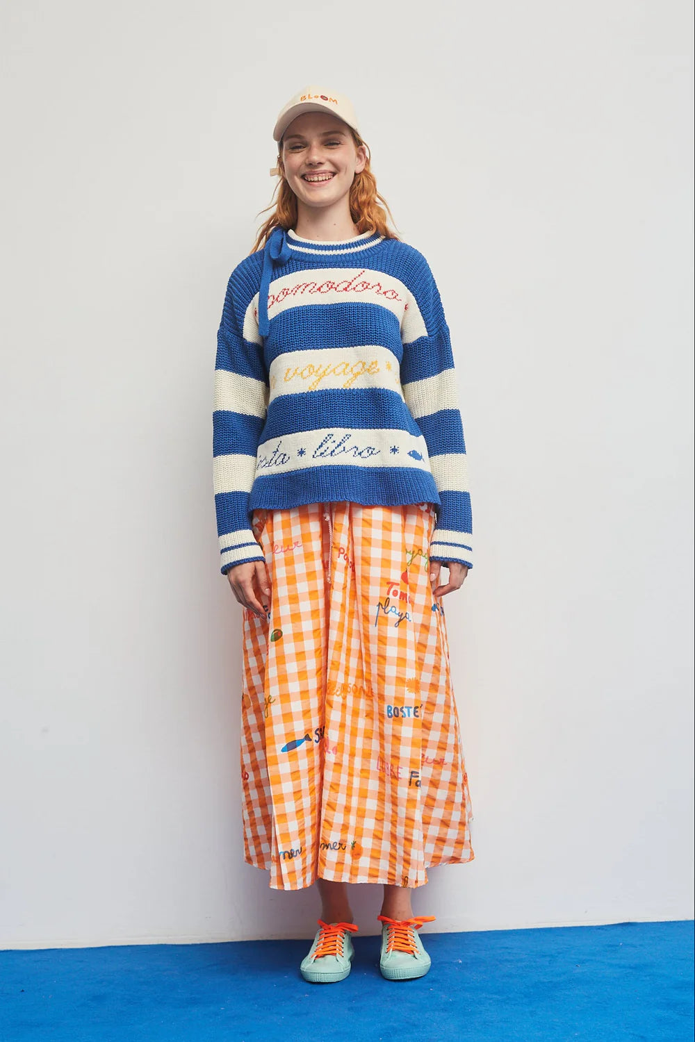 Person wearing a colorful sweater and orange checkered skirt on a white background