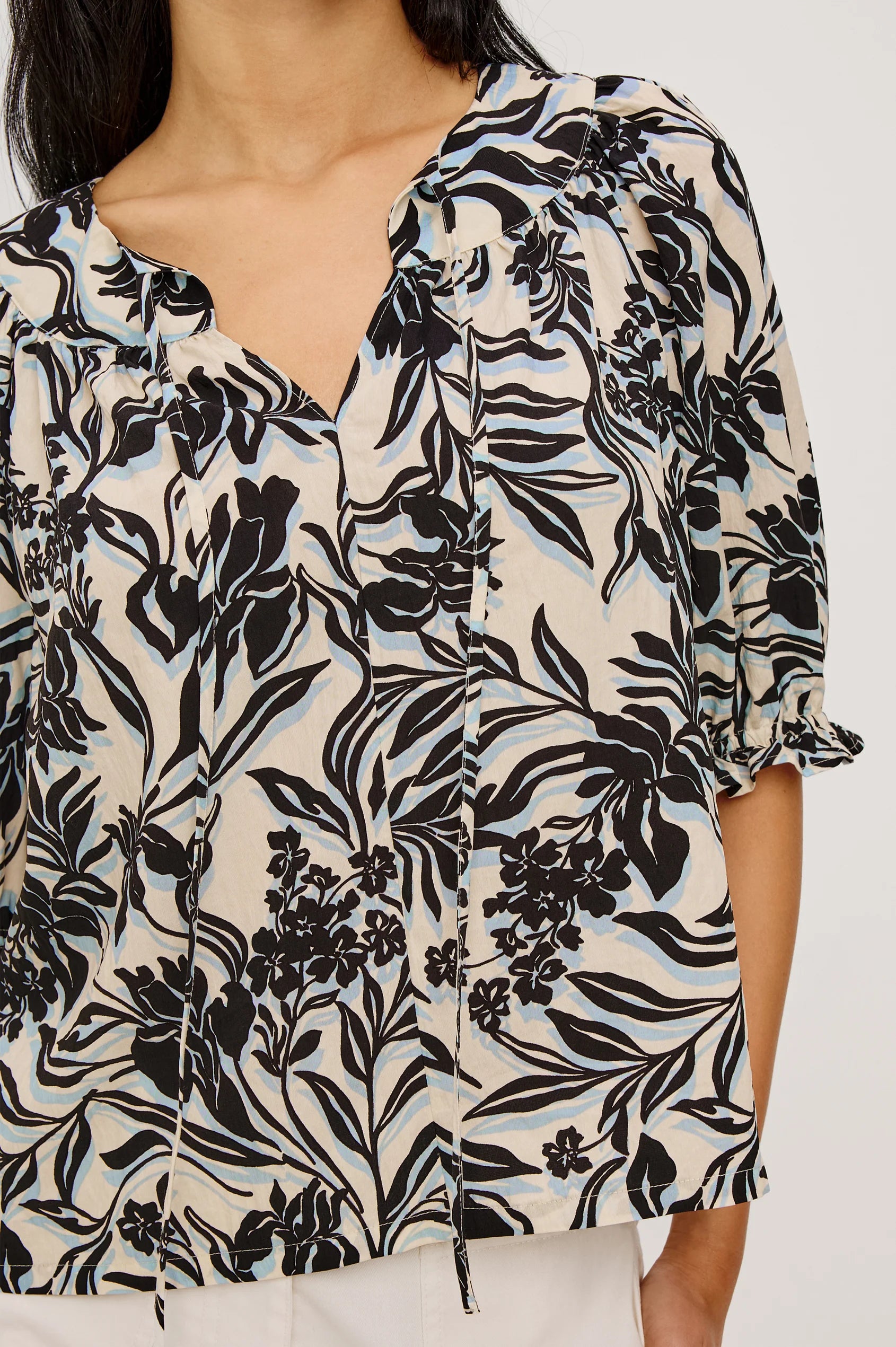 Woman wearing a black and white floral patterned blouse on a plain background