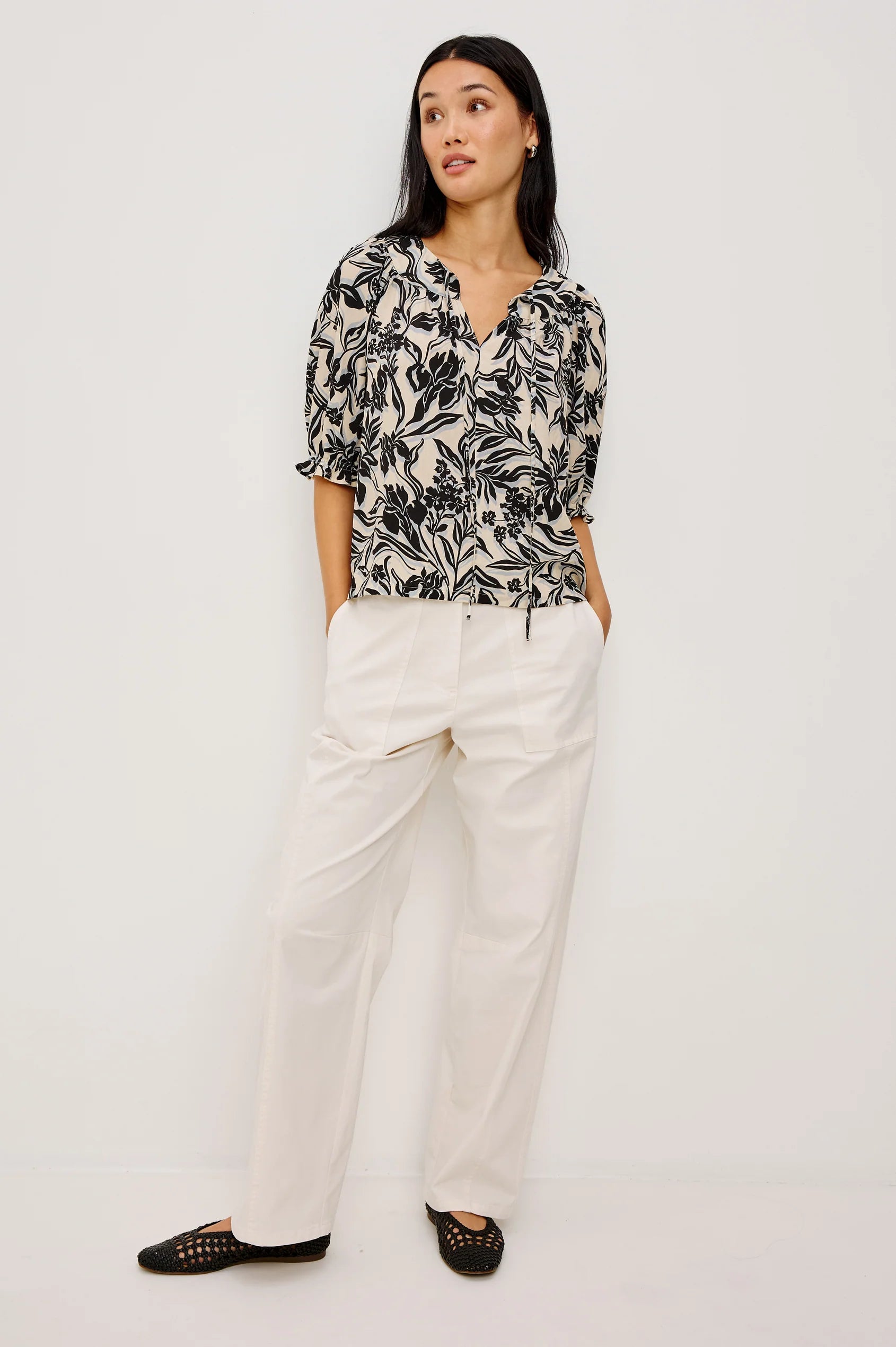 Woman wearing a black and white patterned blouse with white pants on a white background