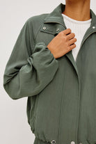 Person wearing a green jacket with a white shirt underneath on a light gray background