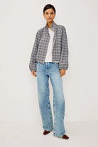 A woman modeling a navy and white checkered long-sleeve cropped jacket with a high stand-up collar, unzipped and full body view paired with light blue jeans, against a plain light gray background.
