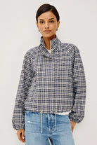 A woman modeling a navy and white checkered long-sleeve cropped jacket with a high stand-up collar, paired with light blue jeans, against a plain light gray background.