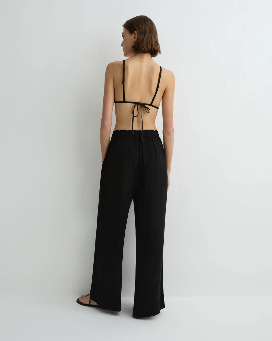 Woman wearing a black strappy top and wide-leg pants on a white background