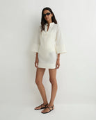 Woman wearing a white outfit with sunglasses on a plain background