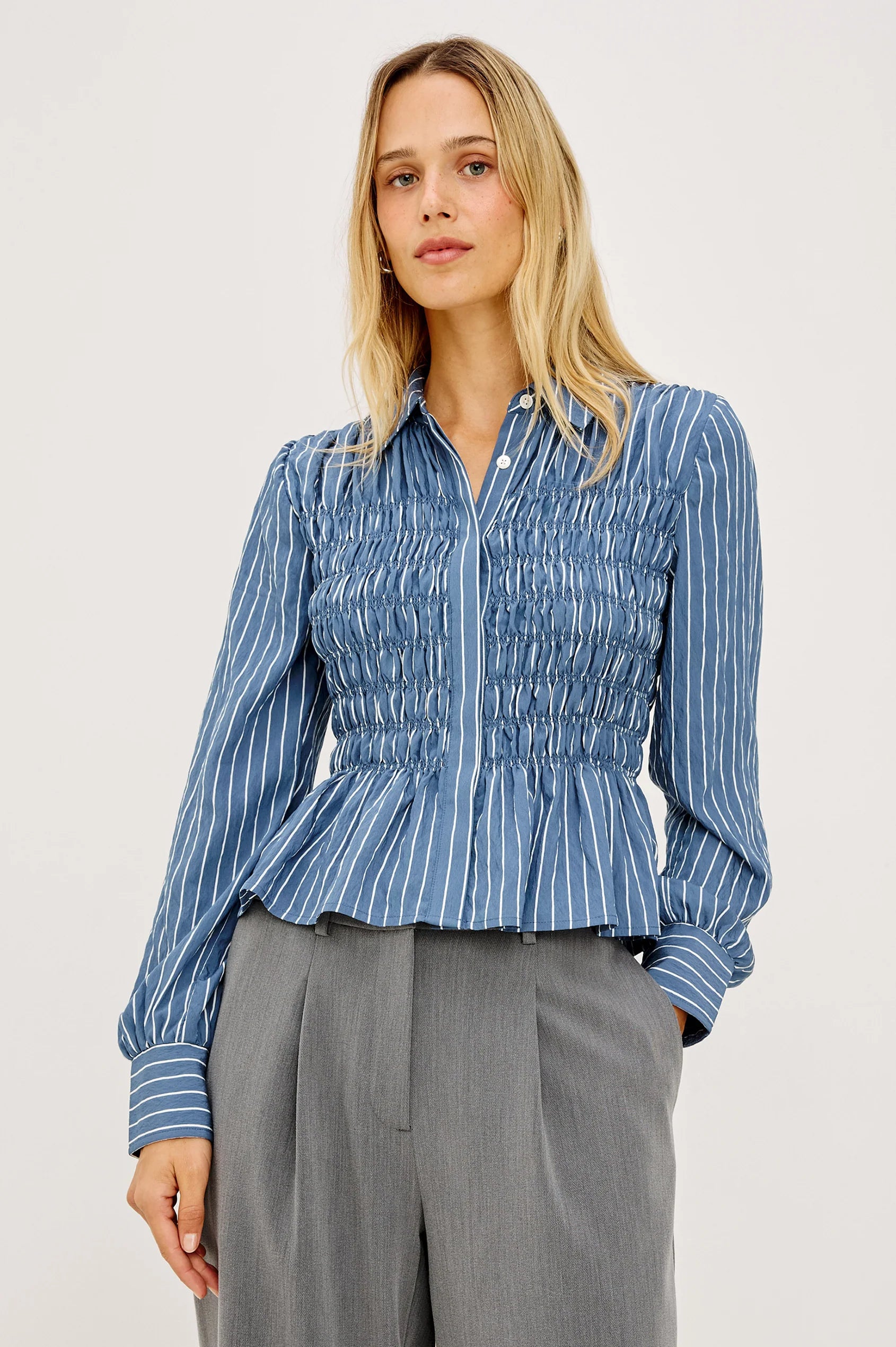 Woman wearing a blue striped shirt and gray pants on a white background
