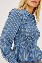 A close-up of a woman wearing a blue long-sleeve blouse with white vertical pinstripes and a smocked bodice, cropped from the mouth down against a plain light background.