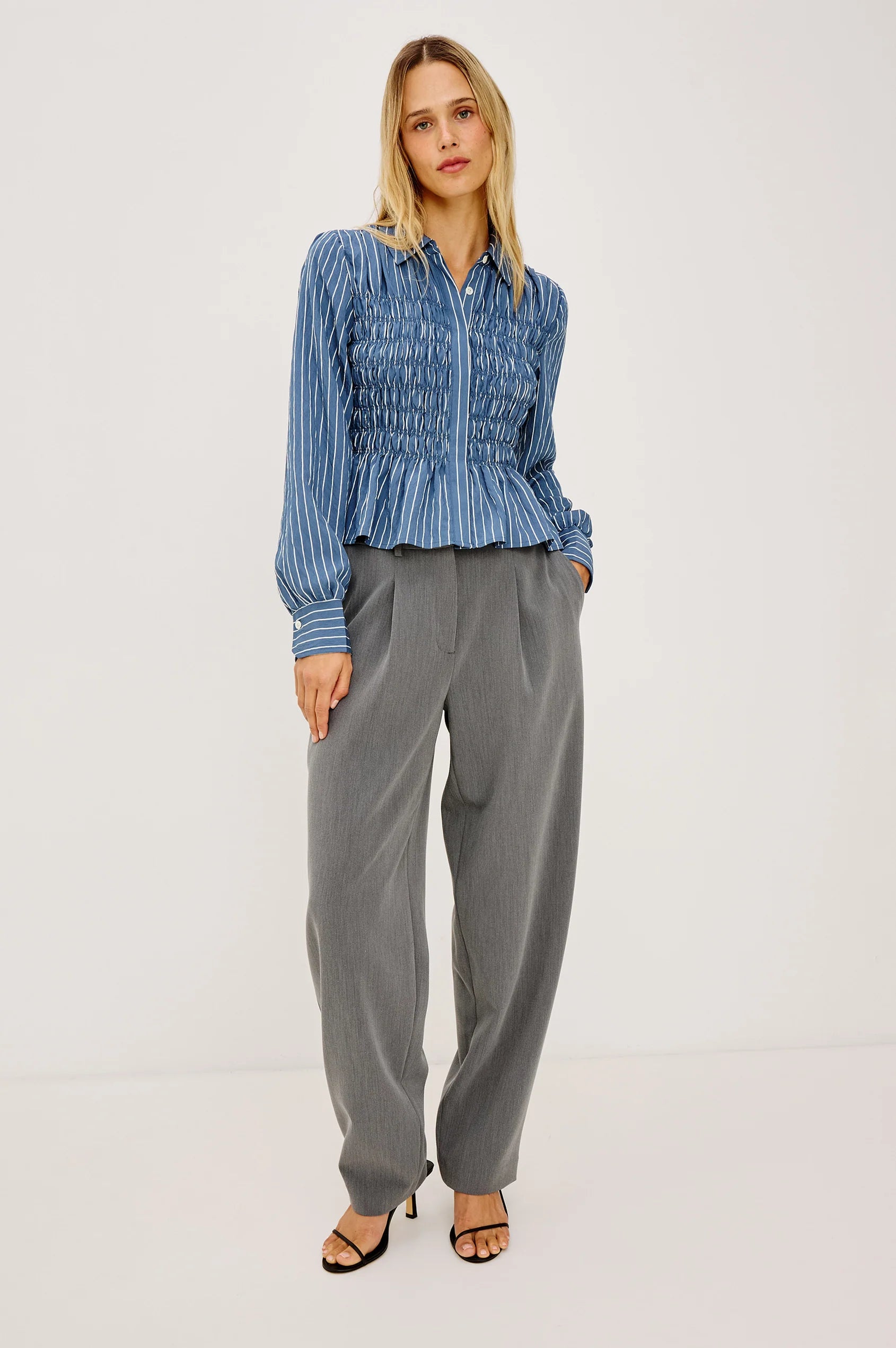 Woman wearing a blue striped shirt and gray pants on a white background