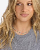Woman wearing a colorful beaded necklace against a neutral background