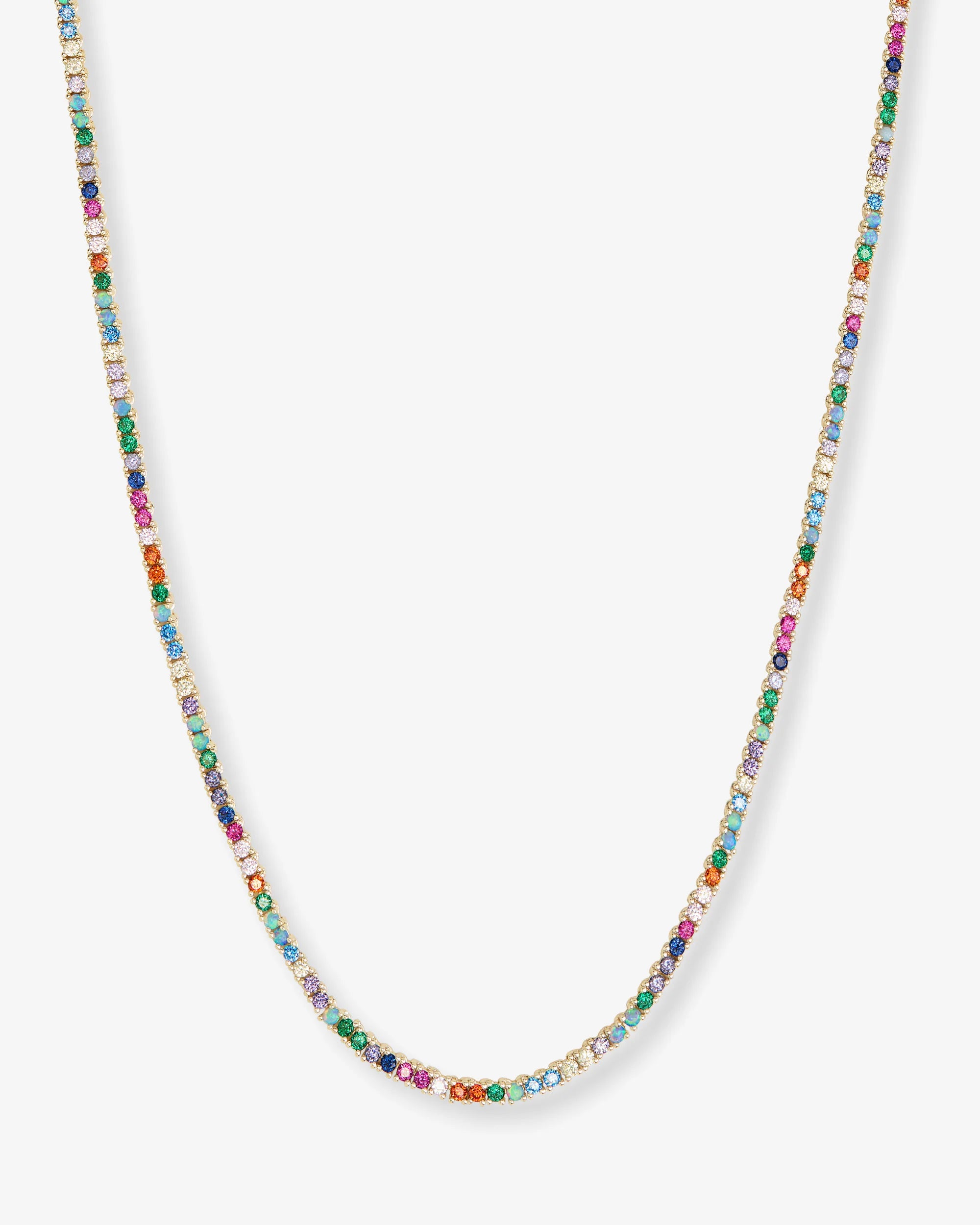 A delicate gold chain necklace adorned with small, colorful gemstones in multiple hues, displayed against a light gray background.