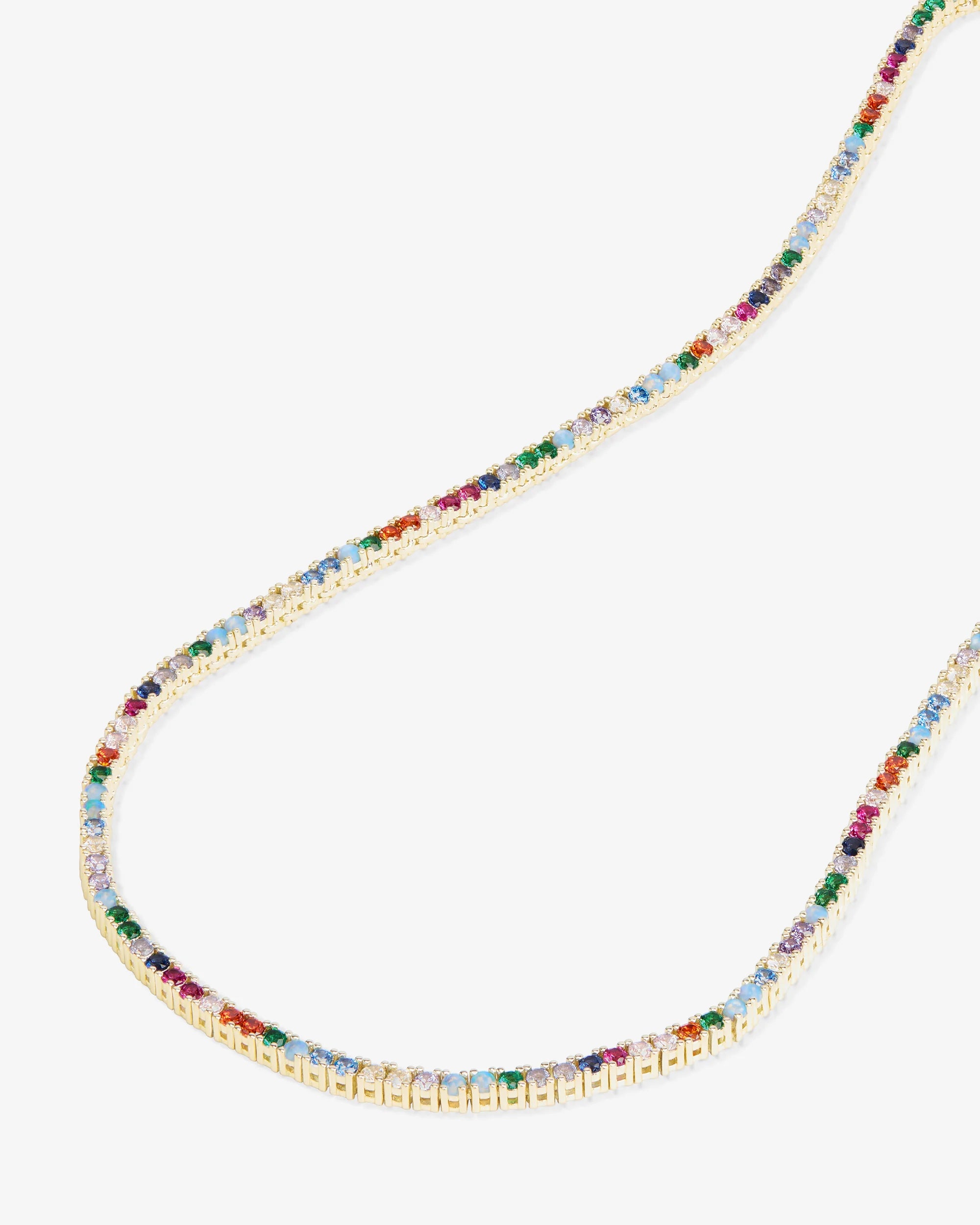 A delicate gold chain necklace adorned with small, colorful gemstones in multiple hues, displayed against a light gray background.