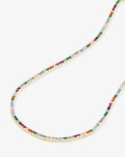 A delicate gold chain necklace adorned with small, colorful gemstones in multiple hues, displayed against a light gray background.