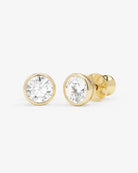 A pair of round-cut diamond stud earrings in yellow gold bezel settings, shown on a clean light gray background.