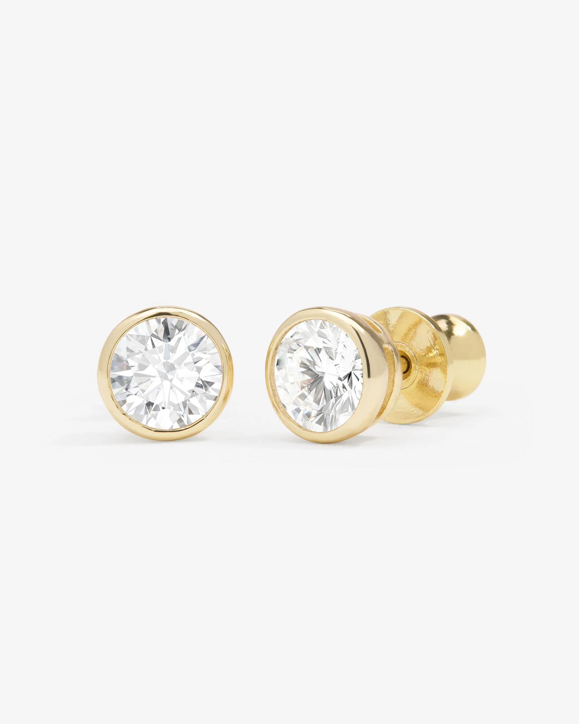 A pair of round-cut diamond stud earrings in yellow gold bezel settings, shown on a clean light gray background.