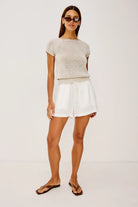 Woman wearing a light gray top and white shorts on a white background