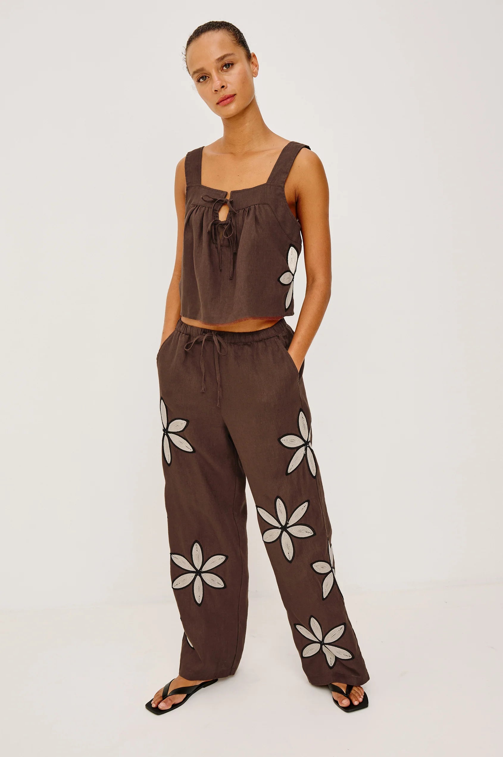 Woman wearing a brown sleeveless top and pants with floral patterns on a white background