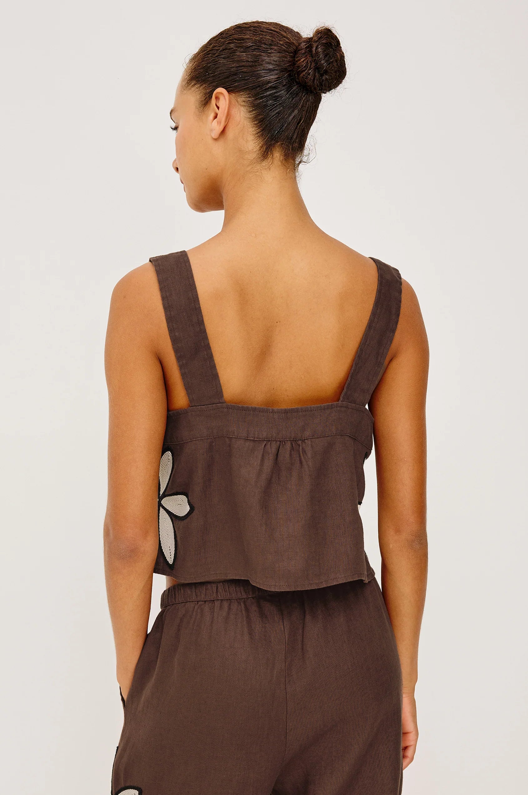 Woman wearing a brown sleeveless top with a floral pattern on a plain background