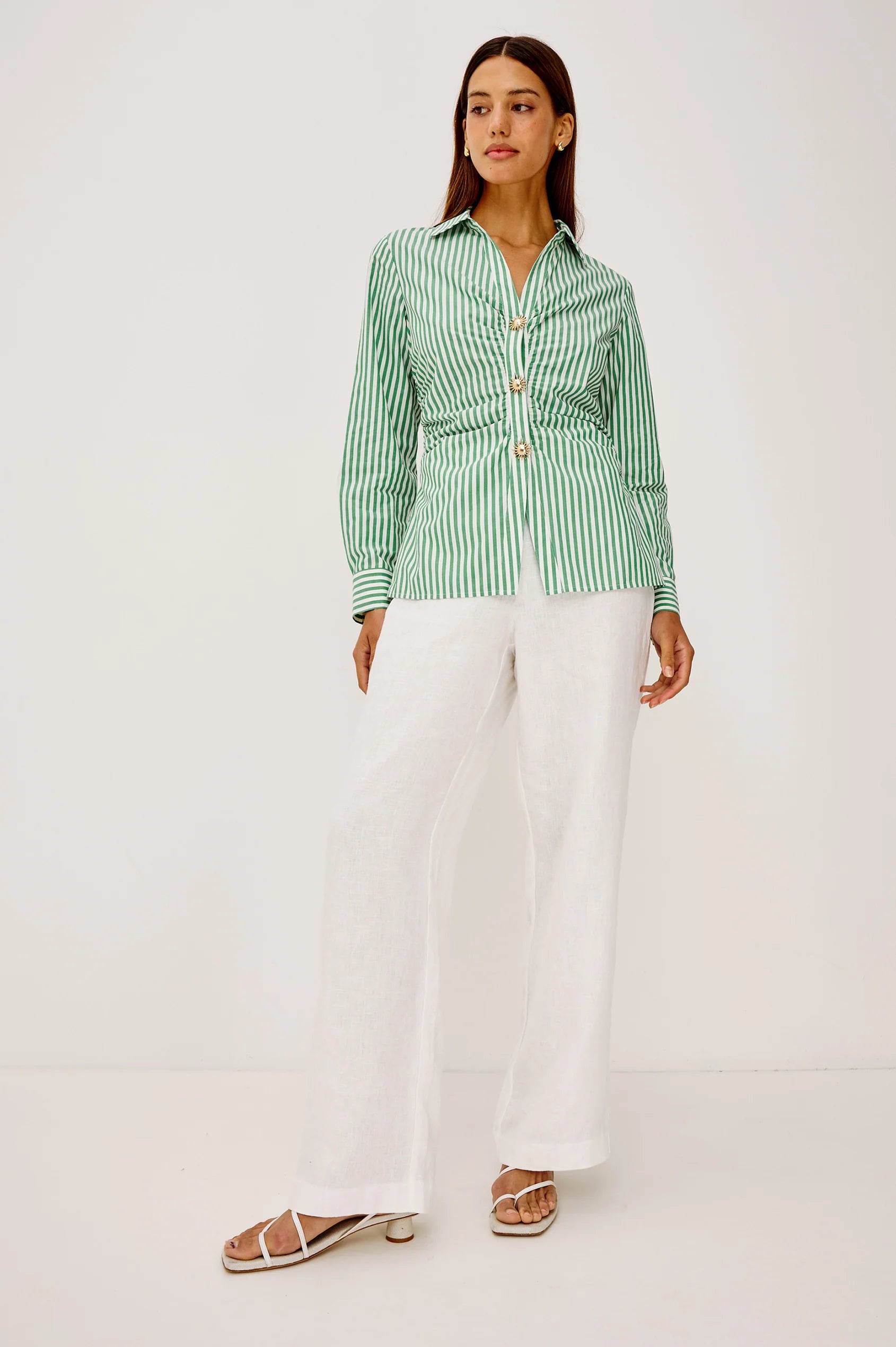 Woman wearing a green and white striped shirt with white pants on a white background