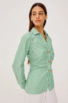 Woman wearing a green and white striped shirt with button details on a light gray background