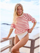 Woman wearing a red and white striped sweater and white swimsuit on a beach.