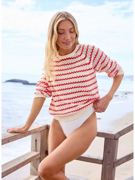 Woman wearing a red and white striped sweater and white swimsuit on a beach.