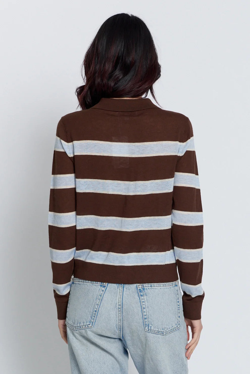 A woman viewed from the back wearing a brown and light gray striped long-sleeve knit top with a mock neck, paired with light-wash jeans, against a plain light gray studio background.