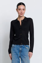 A woman modeling a black long-sleeve knit polo shirt with brown buttons, paired with blue jeans, against a light gray studio background.