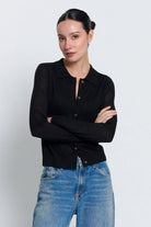 A woman modeling a black long-sleeve knit polo cardigan with brown buttons, paired with blue jeans, against a light gray studio background.