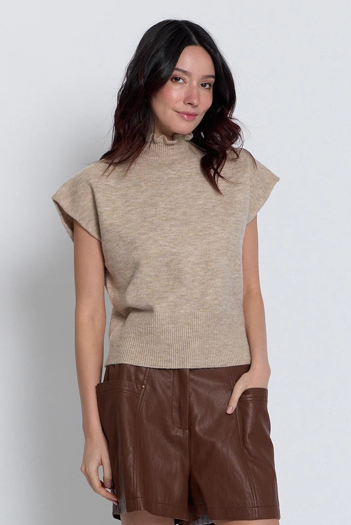 A woman modeling a beige ribbed knit mock-neck top with cap sleeves and brown faux-leather shorts against a light gray studio background.