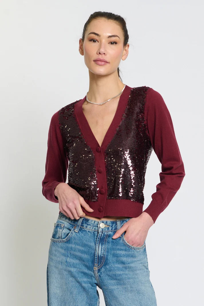 A woman modeling a burgundy long-sleeve cardigan with a sequined front panel, paired with blue jeans, against a plain light gray background.